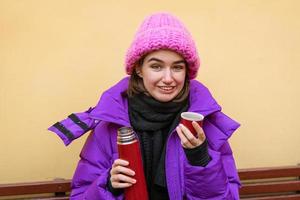 A positive woman spends time outdoors in frosty weather, drinks a hot drink photo