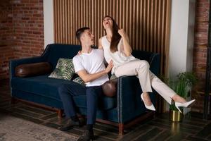 Delighted husband and wife are relaxing on sofa, laughing cheerfully, joking photo