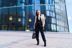 mujer exitosa con anteojos se para frente a un edificio de oficinas con bolsa foto