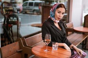 A beautiful woman is sitting in a cafe on the street with a glass of wine photo