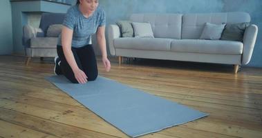 Una mujer deportiva hace ejercicio de tablones en una alfombra gris cerca del sofá en una espaciosa sala de estar a cámara lenta video