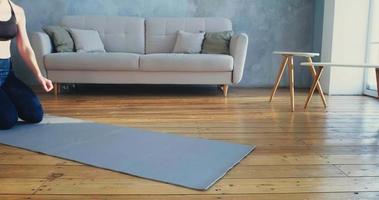 Young sportive woman in stylish tracksuit does plank exercise on grey mat near sofa in spacious living room slow motion video