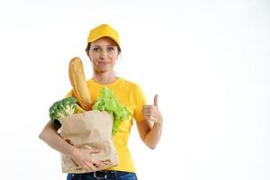 mujer de entrega en amarillo sosteniendo una bolsa de supermercado y dando pulgares hacia arriba, sobre fondo blanco foto