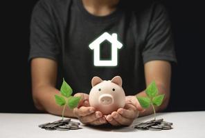 Saving to buy a house or home savings concept with piggy bank on hand and coins photo
