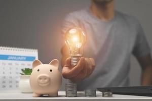 man holding lightbulb on piggy bank and coins stacking on desk. saving money concept photo