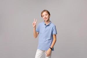 Caucasian young guy in blue shirt happy on light background shows victory photo