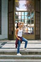 Cute woman in sunglasses poses on the steps in the street near the building photo