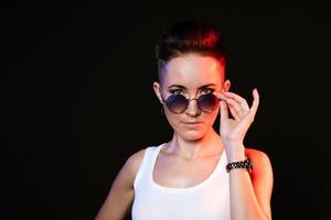 Happy woman in glasses with short hair touches round sunglasses with her hands photo