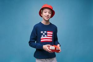 Joyful boy with holiday surprise gift celebrating holiday on blue studio photo