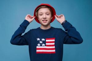 adolescente positivo en suéter azul con bandera de estados unidos y sombrero rojo sonriendo feliz