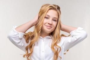 Photo of an optimistic young blonde woman touches her long hair with her hands