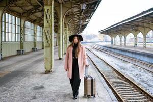 mujer joven con maleta en el andén de la estación. chica viajera esperando foto