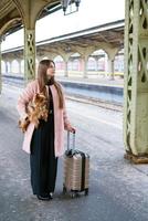 mujer viajera turista camina con equipaje y perro en la estación de tren en rosa foto