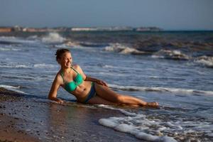 young girl lying on the beach in the surf of the sea in a swimsuit photo