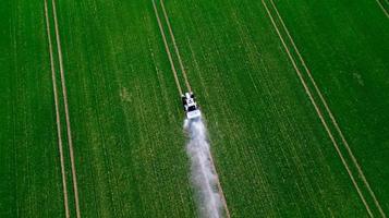 vista aérea del tractor rociando los productos químicos en el gran campo verde foto