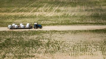 tractor rides on the field and carries bales of hay aerial view photo