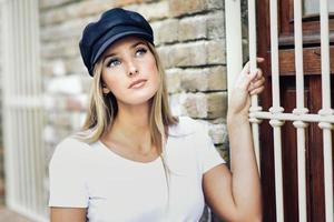 joven mujer rubia con gorra de pie cerca de una pared de ladrillos. foto