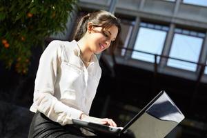 Attractive young businesswoman typing in a laptop computer, urban background photo