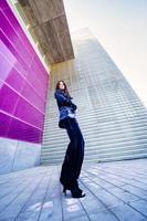 Wide-angle photo of a woman wearing blue suit posing near a modern building.