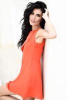 Brunette woman wearing orange short dress in urban background photo