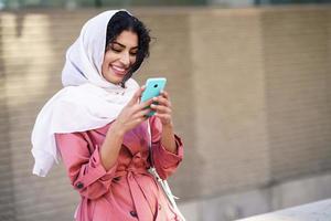 Young Arab woman wearing hijab texting message with her smartphone.
