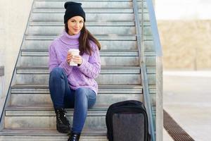 Woman in her twenties taking a coffee break sitting on some steps in the street. photo