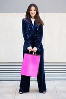 Young woman wearing blue suit carrying several shopping bags near a shopping mall. photo