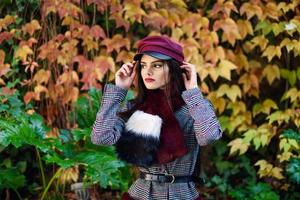 hermosa joven con el pelo muy largo con abrigo de invierno y gorra en el fondo de las hojas de otoño foto