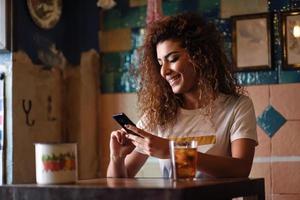 Arabic smiling woman in a beautiful bar looking at her smartphone