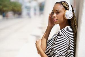 joven negra escuchando música con auriculares inalámbricos al aire libre.