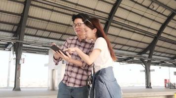 una pareja joven de turistas asiáticos busca información, encuentra lugares de viaje mediante un mapa de tableta en un cruce de la estación de tren en tailandia, estilo de vida de viaje de vacaciones de pasajeros, transporte informal, vacaciones de viaje.