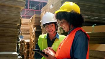 duas trabalhadoras e colegas em uniformes de segurança e verificação de estoque de capacete, controle de produção em armazenamento de fábrica de armazém com muita pilha de papel, amigo trabalha em negócios de fabricação de reciclagem. video