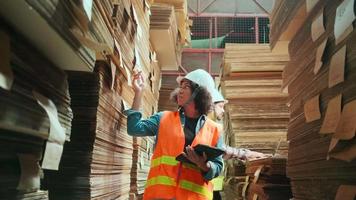 la lavoratrice afroamericana in uniforme di sicurezza e elmetto e collega di sesso maschile ispezionano lo stoccaggio, l'ordine di scorta nel magazzino di fabbrica, le pile di carta impilata, la gestione dei prodotti industriali. video