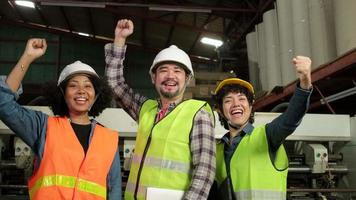 três trabalhadores de engenheiros de uniforme de segurança e capacetes após o trabalho comemoram, mãos levantadas juntas, felizes e alegres, trabalhos da indústria bem-sucedidos, conquista, fábrica de fabricação de técnicos profissionais. video