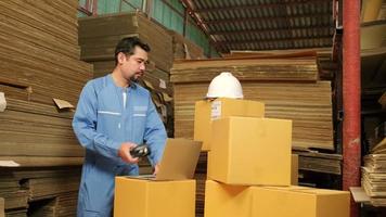 Asian male worker in safety uniform and hard hat using bar code scanner to check shipping orders at parcels warehouse, paper manufacture factory for the packing industry, logistic transport service. video