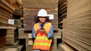 Warehouse female worker in safety uniform mobile phone addicts works idle, male manager orders to check supply stocks in industrial factory, piles of stacking paper manufacture, product distribution. video