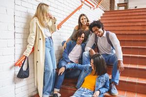 Group of students with ethnic variety, sitting on some street steps having fun together. photo