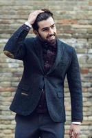 Young bearded man smiling in urban background wearing british elegant suit in the street. photo