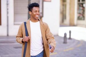 Happy black man walking down the street carrying a briefcase and a smartphone in his hand. photo