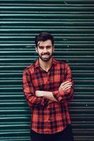 Young bearded smiling man wearing a plaid shirt with a green blind behind him. photo