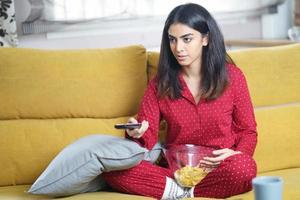 Persian woman at home watching TV and using remote control photo