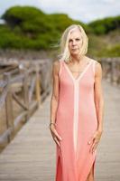 Beautiful mature woman walking along a wooden path near the beach., wearing a nice orange dress. photo