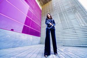 Wide-angle photo of a woman wearing blue suit posing near a modern building.