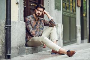 Young bearded man, model of fashion, sitting in an urban step wearing casual clothes. photo