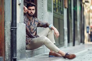 Young bearded man, model of fashion, sitting in an urban step wearing casual clothes. photo