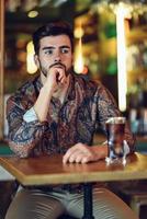 Thoughtful bearded man wearing casual clothes sitting in a modern pub. photo