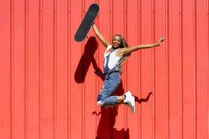 Carefree black woman with skateboard jumping in city photo