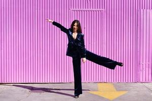 Woman wearing blue suit dancing near pink shutter. photo