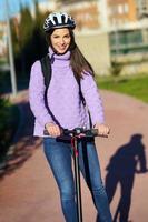 Young woman in her twenties riding an electric scooter using helmet. photo