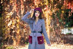 joven hermosa chica con abrigo y gorra en el fondo de las hojas de otoño. foto